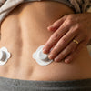 Pressing one white pod onto the right side of the lower back, the second pod already in place