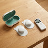 Top view: the open charging case, the two pods on their gel pads and the slim remote