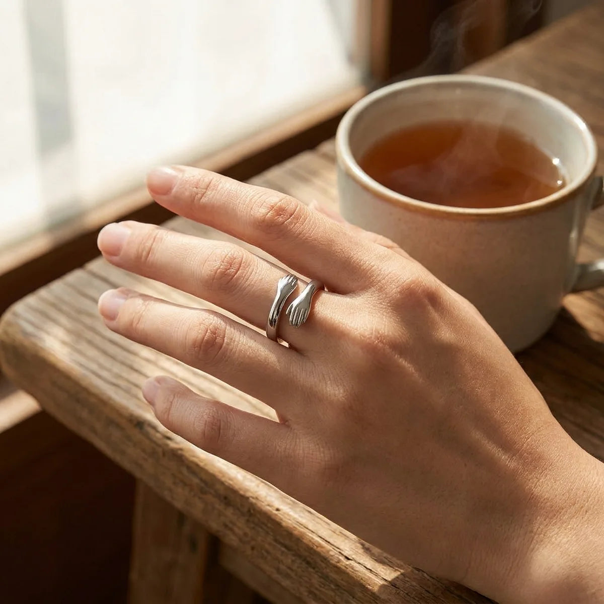 The Hug Ring worn on a woman's finger at a table