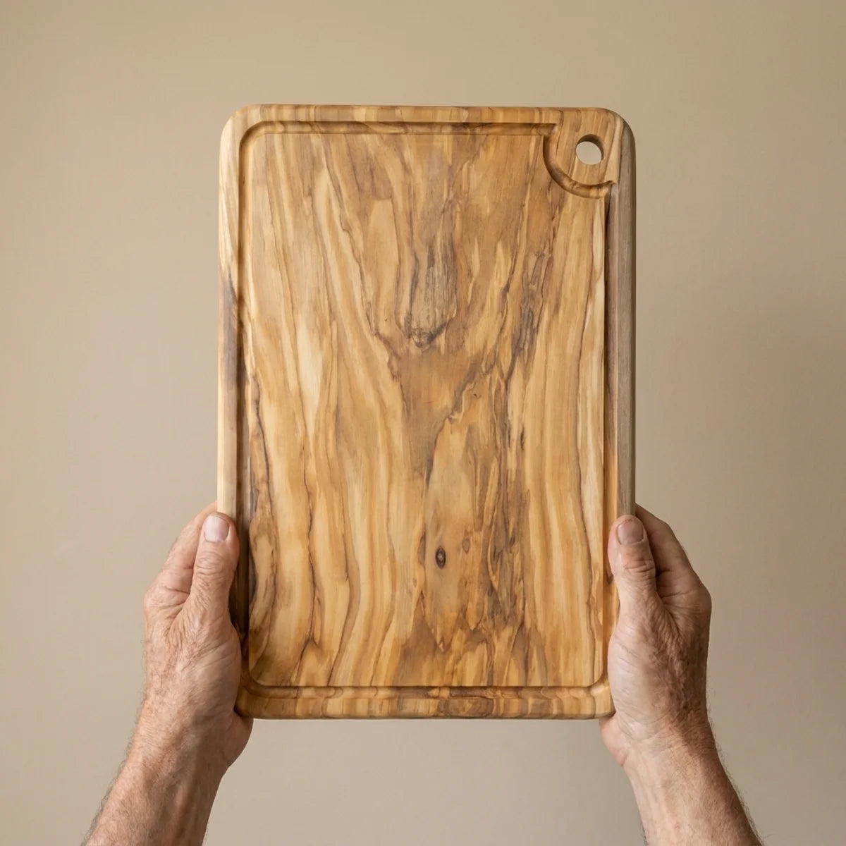 The Alba Olive Wood Carving Board with Juice Groove held in two hands, showing its size