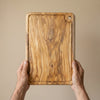 The Alba Olive Wood Carving Board with Juice Groove held in two hands, showing its size