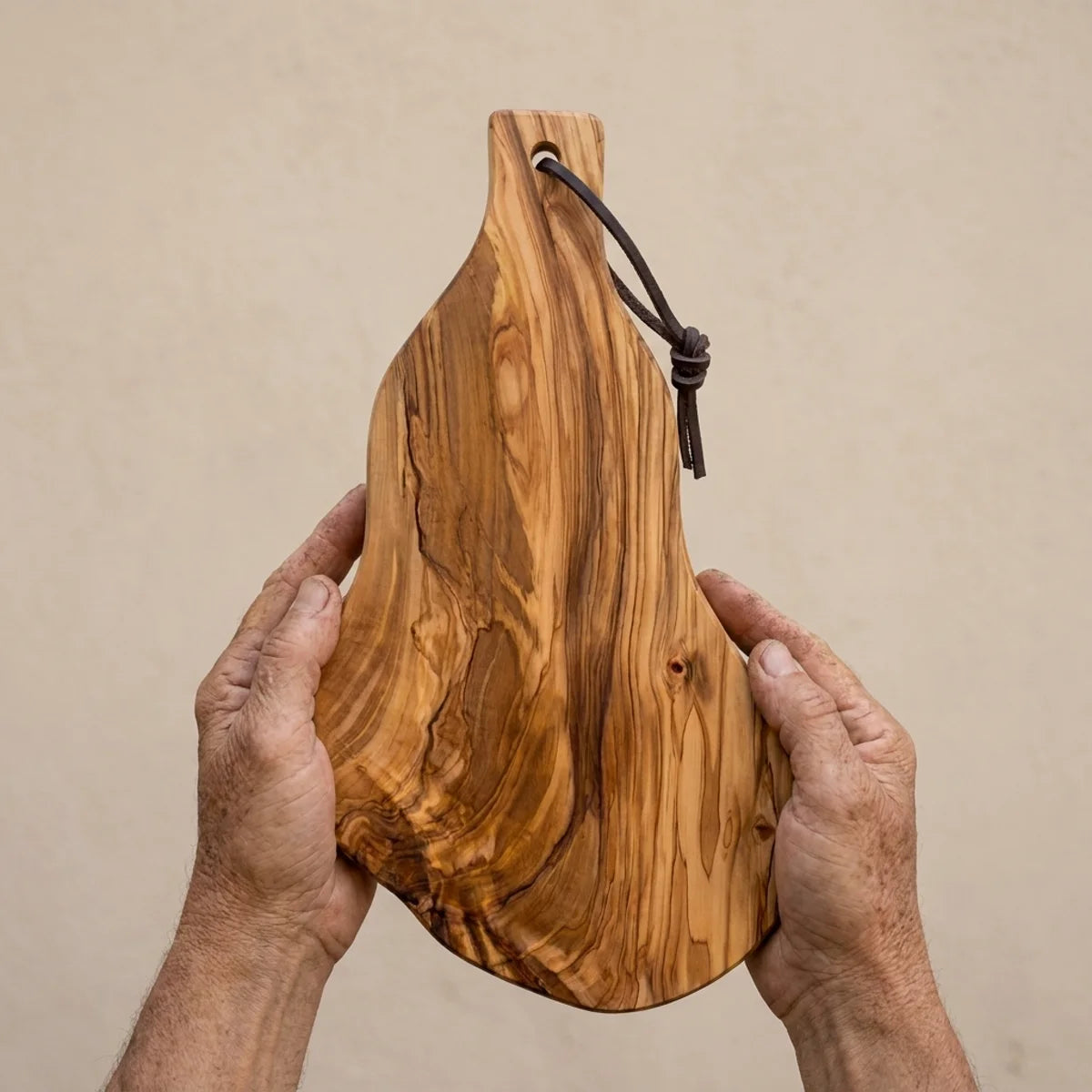 The Alba Olive Wood Board with Leather Loop held in two hands, showing its size