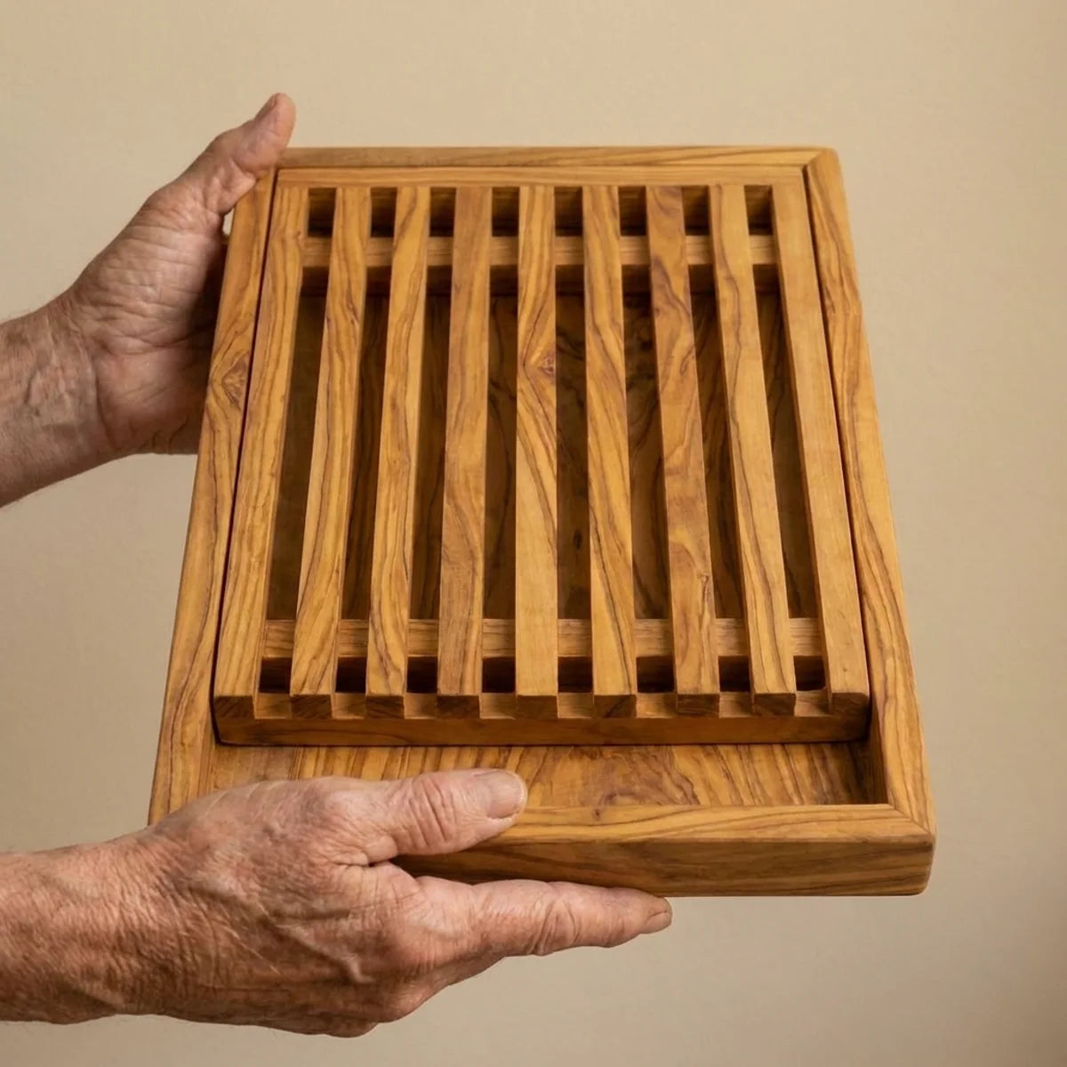 The Alba Olive Wood Bread Board with Crumb Tray held in two hands, showing its size