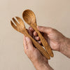 The Alba Olive Wood Serving Set (Fork + Spoon) held in two hands, showing its size