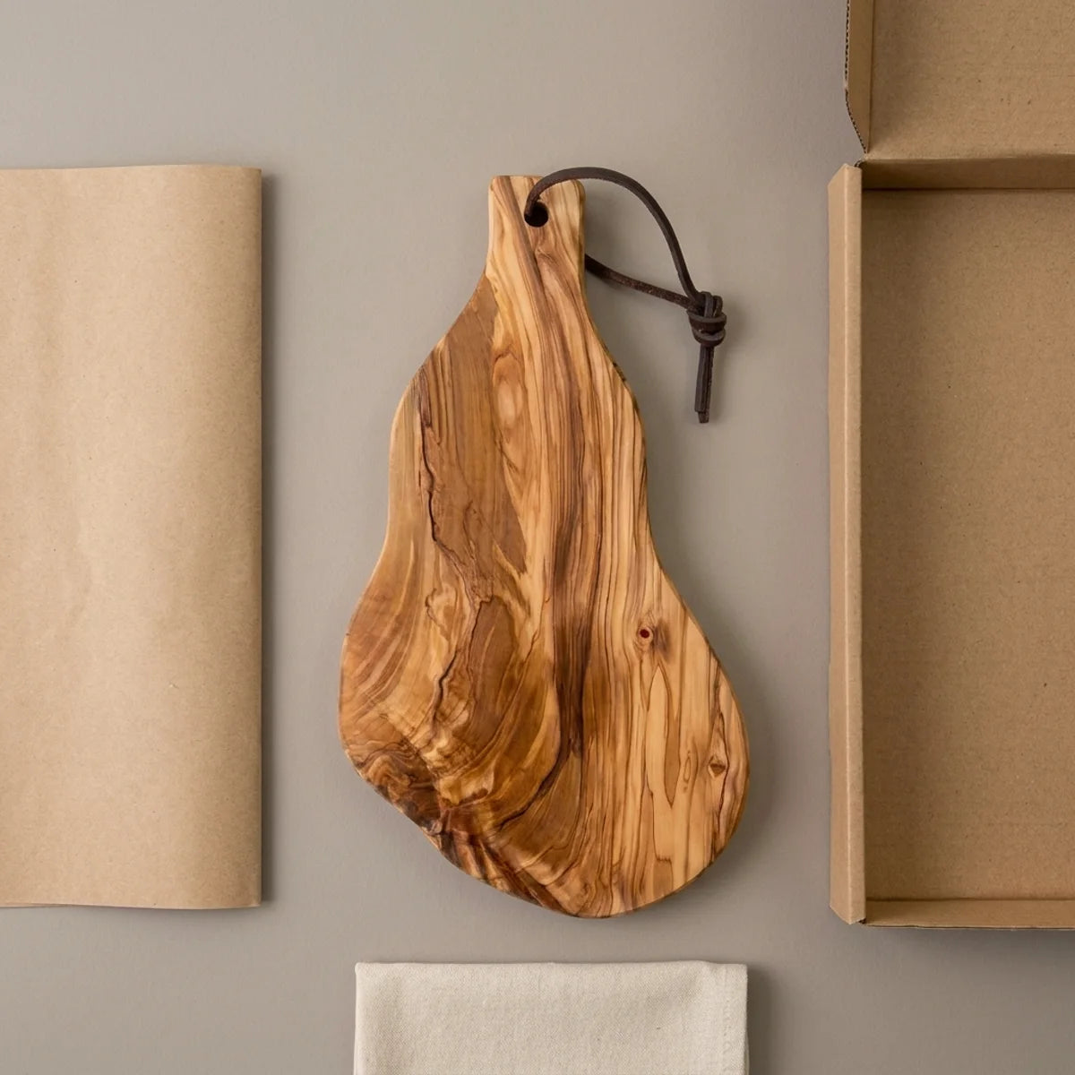 The Alba Olive Wood Board with Leather Loop with its kraft wrapping and plain shipping box