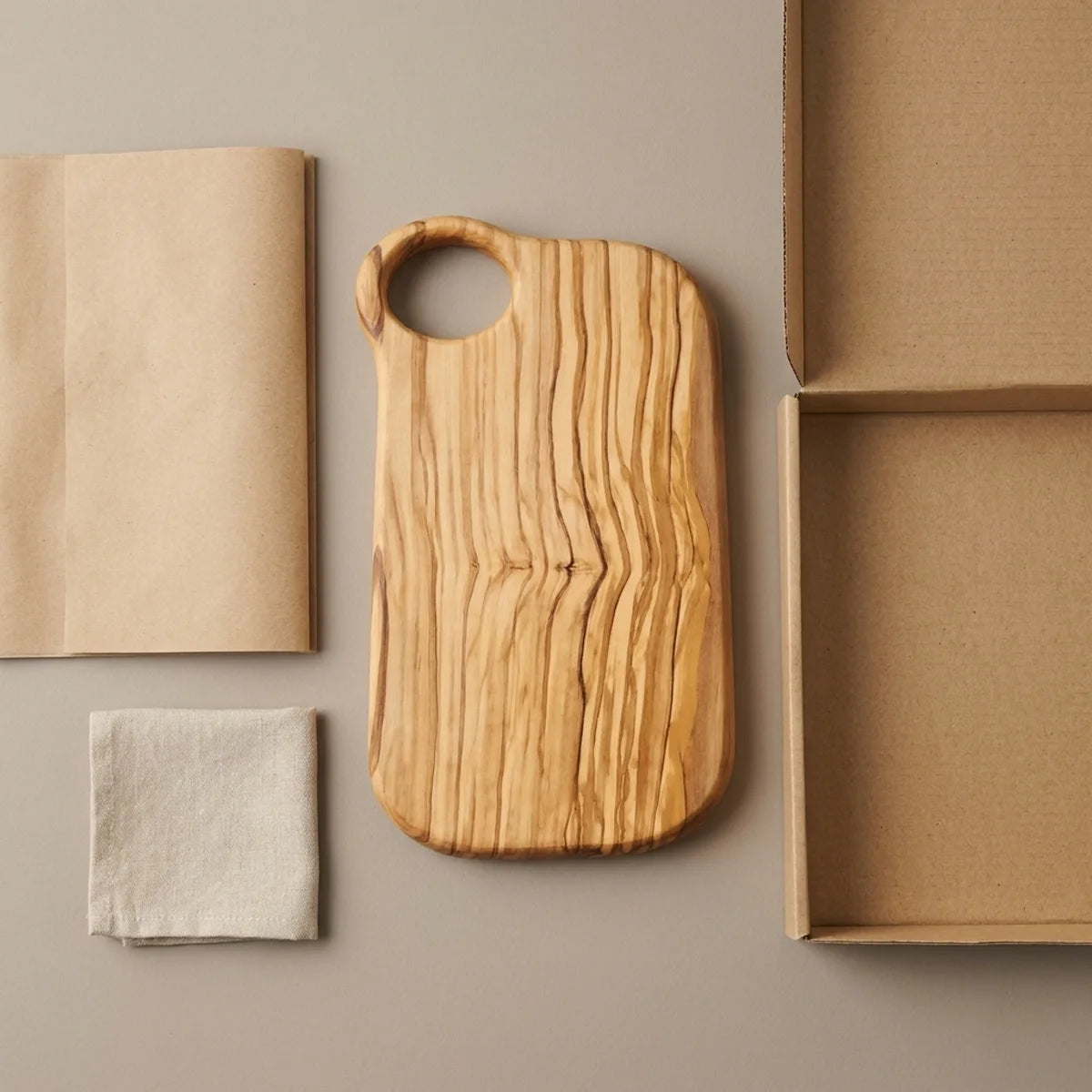 The Alba Olive Wood Board with Grip Hole with its kraft wrapping and plain shipping box